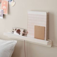 a white shelf with a notebook and other items on it next to a wall mounted clock