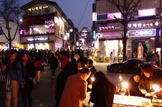 a group of people standing around a table with candles on it in the middle of a street