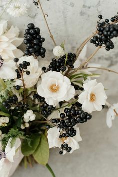 white flowers and black berries are arranged in a vase on a marble surface with text overlay