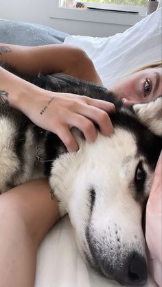 a woman laying on top of a bed next to a husky dog with her eyes closed