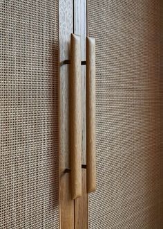 a wooden door handle on the side of a wood paneled wall with woven fabric behind it