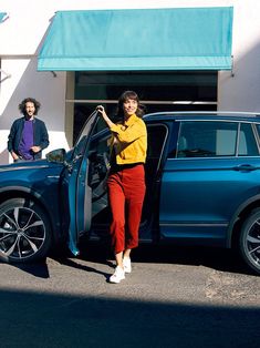 a woman standing next to a blue car in front of a building with two men