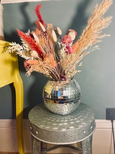 a disco ball sits on top of a stool next to a mirror vase filled with flowers