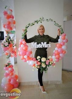 a woman standing in front of balloons with the word mom on it and flowers around her