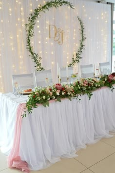 the table is set up with white chairs and pink sashes, greenery and candles