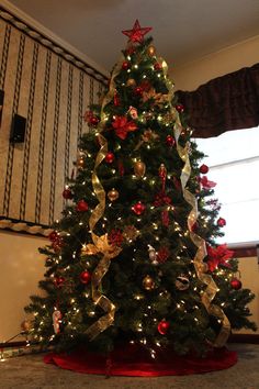 a christmas tree is decorated with red and gold ribbons, bows, and baubles