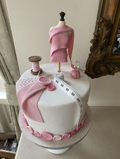 a white cake with pink decorations and sewing supplies on top, sitting in front of a mirror