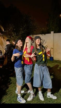 three young women standing next to each other on top of a lush green field at night