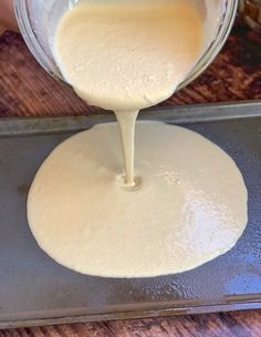 someone is pouring batter on top of a pizza crust in a glass bowl over a cookie sheet