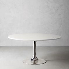 a white table with an oval top and metal base in front of a plain wall