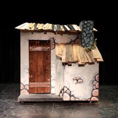 a small house made out of wood and painted with designs on the side, sitting in front of a black curtain