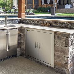 an outdoor kitchen with stainless steel appliances and grilling area next to swimming pool in the background