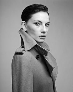 a black and white photo of a woman in a trench coat looking at the camera