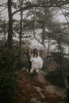 a bride and groom walking down a path in the woods with an umbrella over their heads