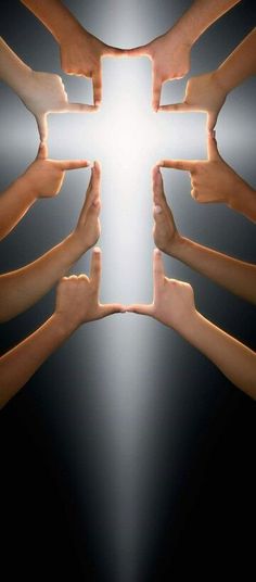 several hands reaching towards a cross in the middle of a dark room with light coming through it