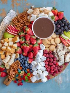 a platter filled with fruit, crackers, and other snacks on a blue surface