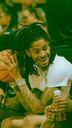 a man with dreadlocks sitting on the floor holding a basketball in his hand