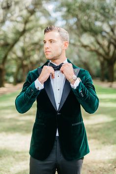 a man in a green velvet jacket adjusting his bow tie