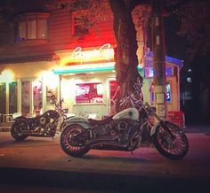 two motorcycles are parked in front of a building at night with neon lights on the windows