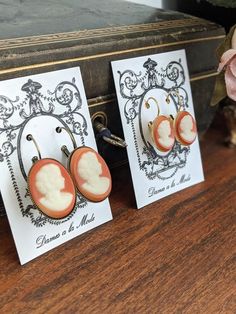 These are classical cameo styles!  A cream silhouette against a coral orange ground!  These are high-quality glass cameos. The cameos are available in two sizes: Larger 25mm or smaller 18mmThey are set in nickel-free leverback settings in your choice of Gold (smaller cameo shown in this finish), Antique Gold (larger cameo shown in this finish), Silver, or Antique Silver. Lots more Georgian- and Regency-inspired jewelry is available in my shop at Dames a la Mode: https://www.etsy.com/shop/damesal Cameo Earrings, Cameo Jewelry, Vintage Cameo, Leverback Earrings, Coral Orange, Inspired Jewelry, Earrings Vintage, Jane Austen, Vintage Earrings