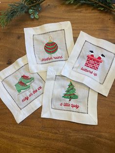 four embroidered christmas napkins on top of a wooden table