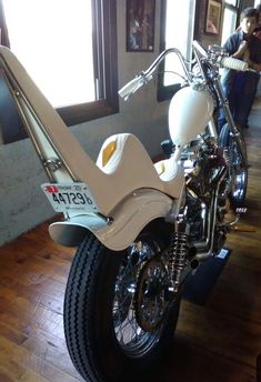 a white motorcycle parked inside of a building next to a wooden floor with people looking in the window