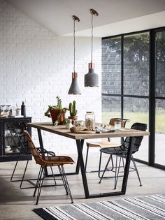 a dining room table with chairs and lights hanging from it's ceiling, in front of a brick wall