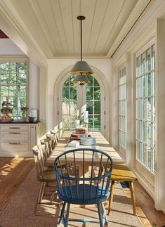 a long table with blue chairs in the middle of a dining room filled with lots of windows