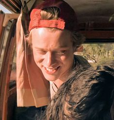 a woman sitting in the back seat of a car with her head down and wearing a red bandana