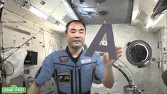 a man in a space suit holding up a letter shaped like a 4 on the inside of a space station