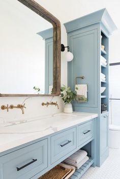 a bathroom with blue cabinets and a large mirror above the sink is shown in this image