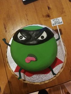 a green cake with a black mask on top and a sign that says it's okay to get pregnant