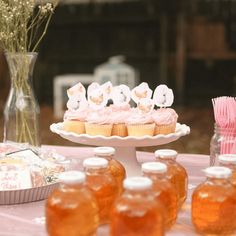 cupcakes and honey jars on a table with flowers in vases behind them