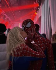 a woman dressed as spider - man kissing another woman's face in front of a crowd