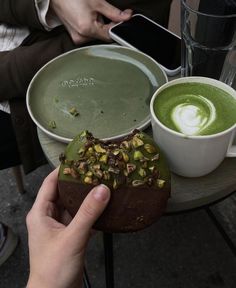 a person holding up a piece of cake next to a cup of green liquid on a table