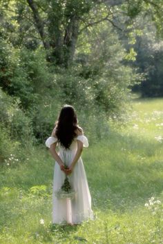 a woman in a white dress is standing in the grass with her back to the camera