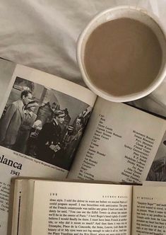 an open book sitting on top of a bed next to a cup of coffee