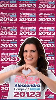 a woman making a heart shape with her hands while standing in front of a pink background