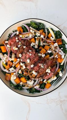 a bowl filled with meat and vegetables on top of a white countertop next to a fork