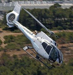 a white helicopter flying over a lush green hillside