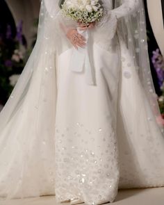 a woman in a white wedding gown and veil holding a flower bouquet on the runway