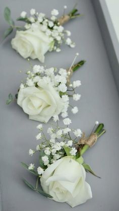 three white roses and baby's breath are arranged in a row on a gray surface