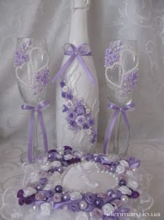 a bottle and two wine glasses on a lace tablecloth with purple ribbons around it