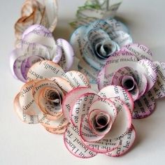 several rolled up paper flowers sitting on top of a white tablecloth covered surface with words written all over them