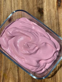 a square glass container filled with pink icing on top of a wooden table next to a knife