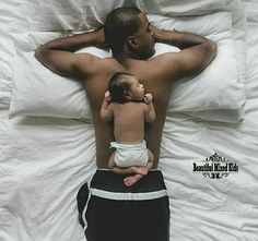 a man laying in bed holding a baby next to him on top of a pillow