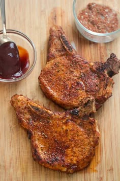 two pieces of meat sitting on top of a wooden cutting board next to dipping sauce