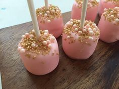 pink cake pops with gold sprinkles and white candles on a wooden table