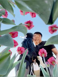 a man and woman kissing in front of pink flowers