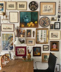 a wooden table topped with lots of framed pictures and art on the wall above it